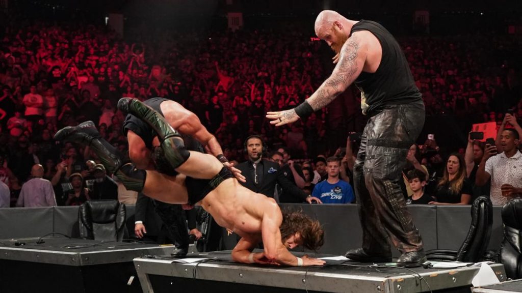 Daniel Bryan hurricanrana's Luke Harper off an announce desk, with Erick Rowan standing on the desk