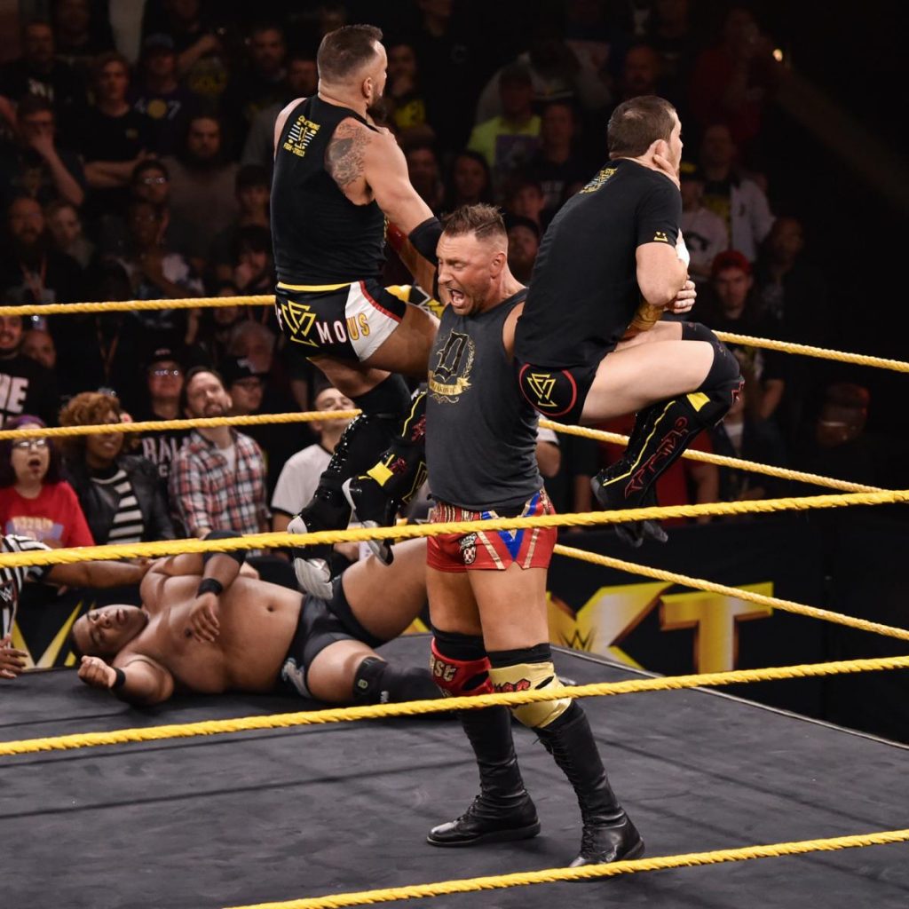 Dominik Dijakovic holding Bobby Fish and Kyle O'Reilly above his head, one in each hand