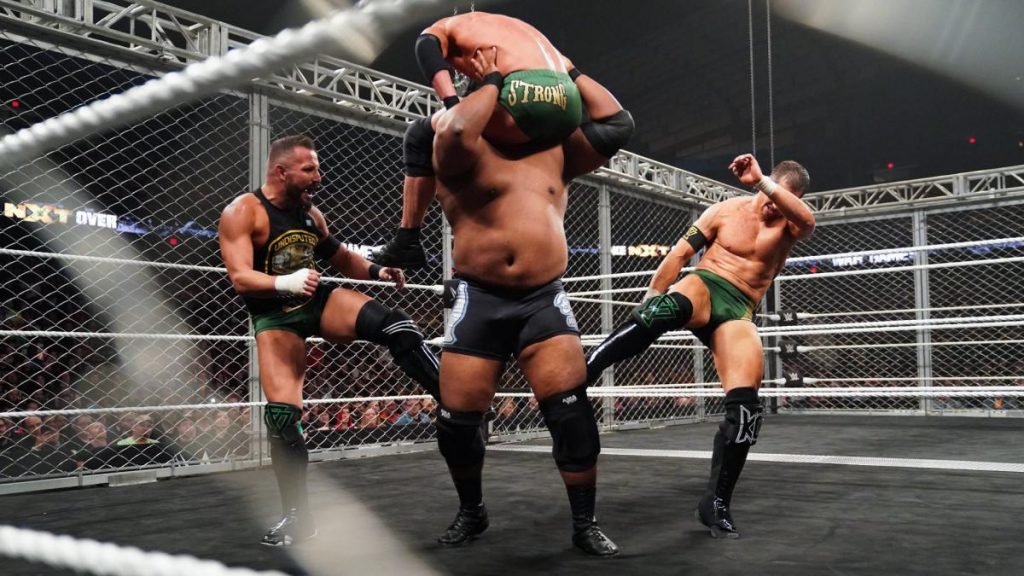 Undisputed ERA's Bobby Fish and Kyle O'Reilly kick the backs of Keith Lee's knees to stop him spirit bombing Roderick Strong