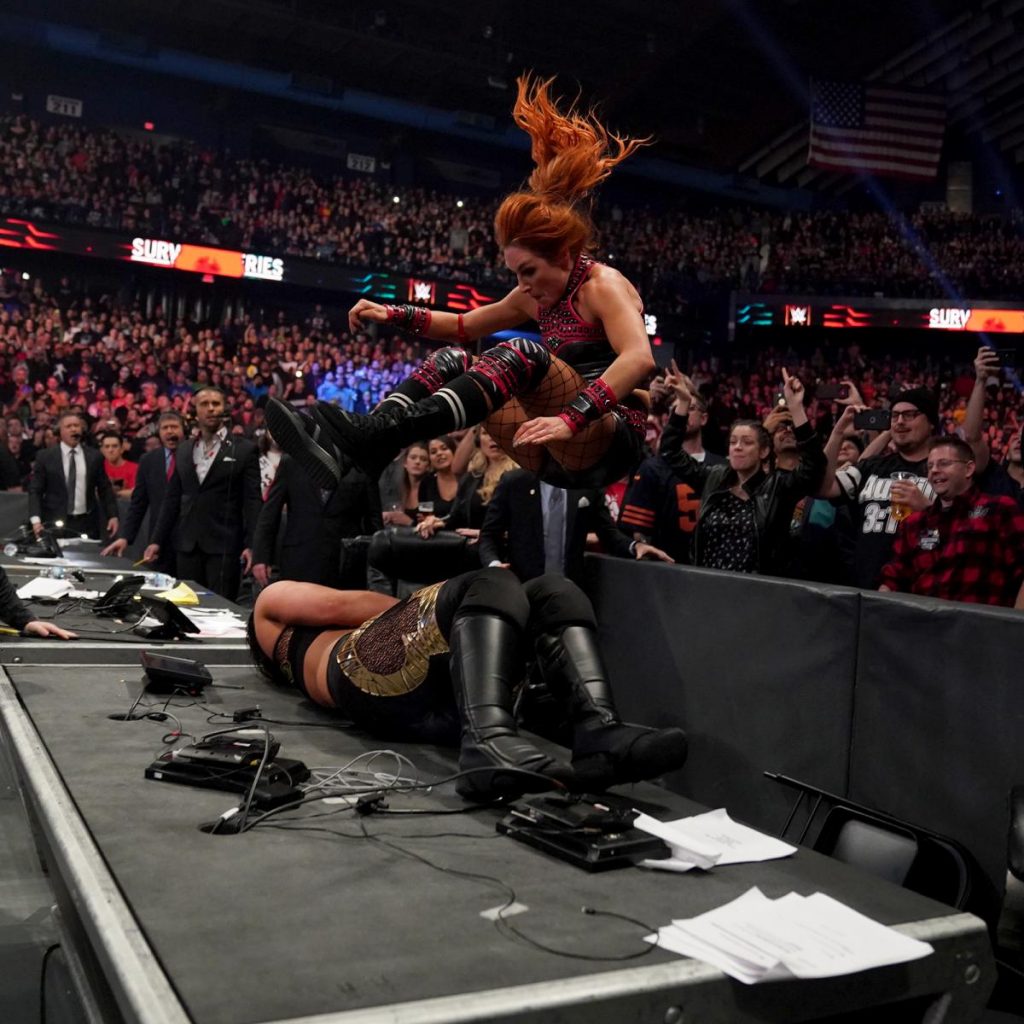 Becky Lynch leg drops Shayna Baszler through an announce desk from the barricade