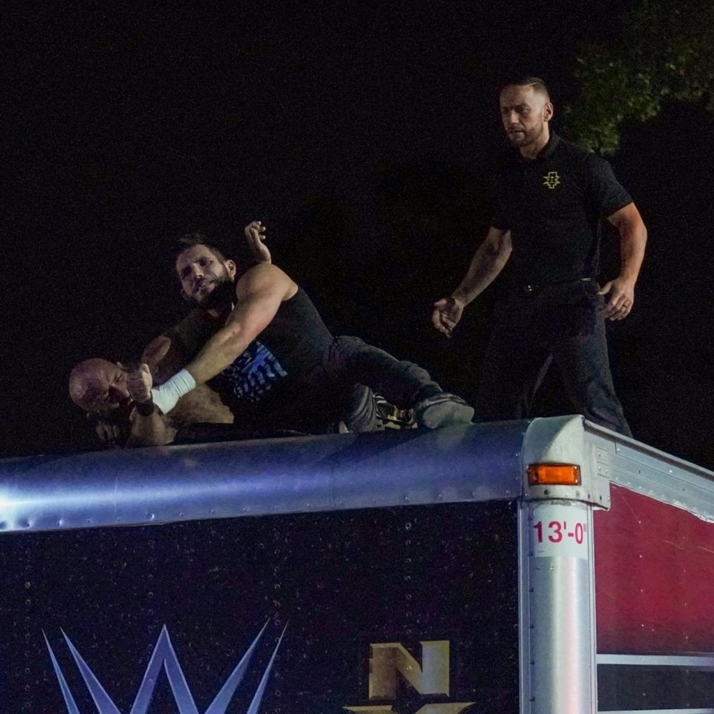 Johnny Gargano and TOmmaso Ciampa fight on top of a truck while the ref watches on
