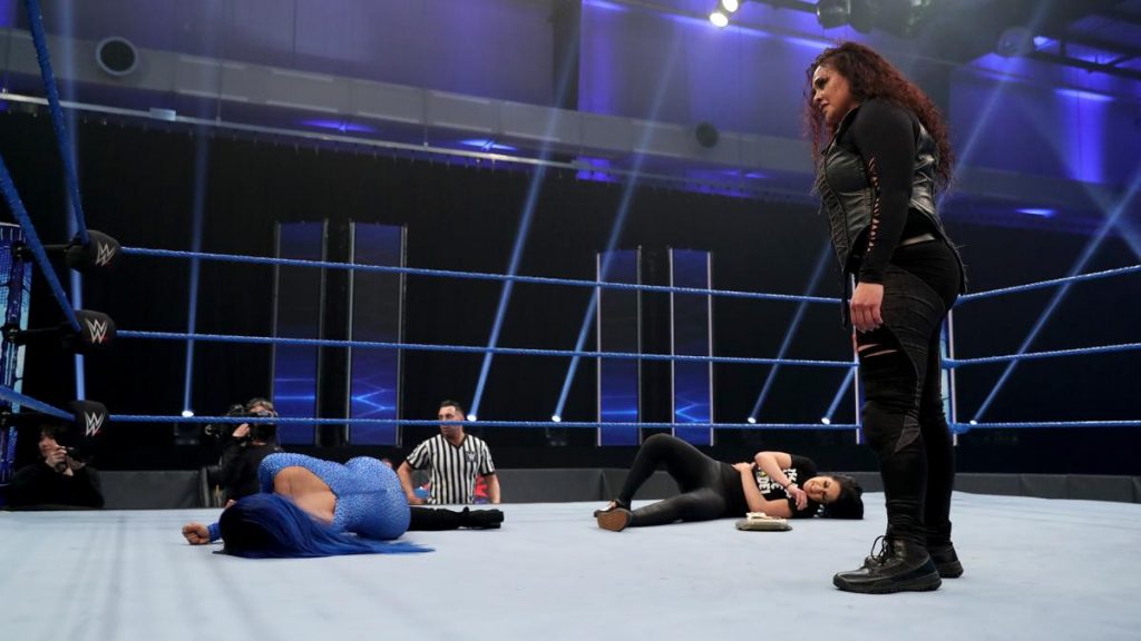 Tamina looks down at Sasha Banks and Bayley after laying them out.