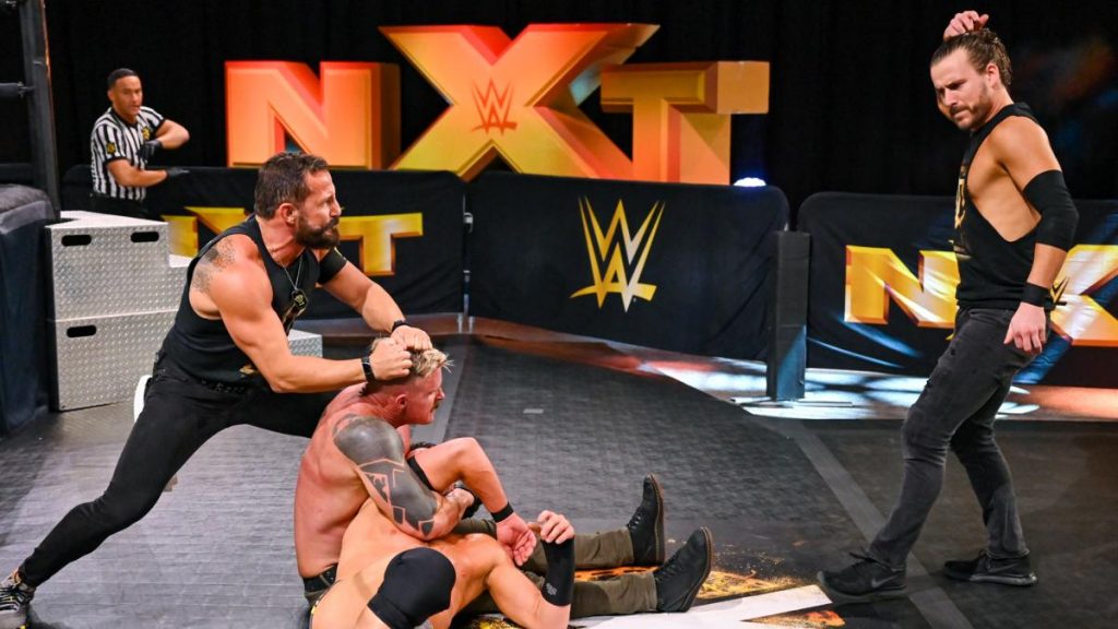 Bobby Fish holds Dexter Lumis still for Adam Cole so he can try to make him let go of Roderick Strong