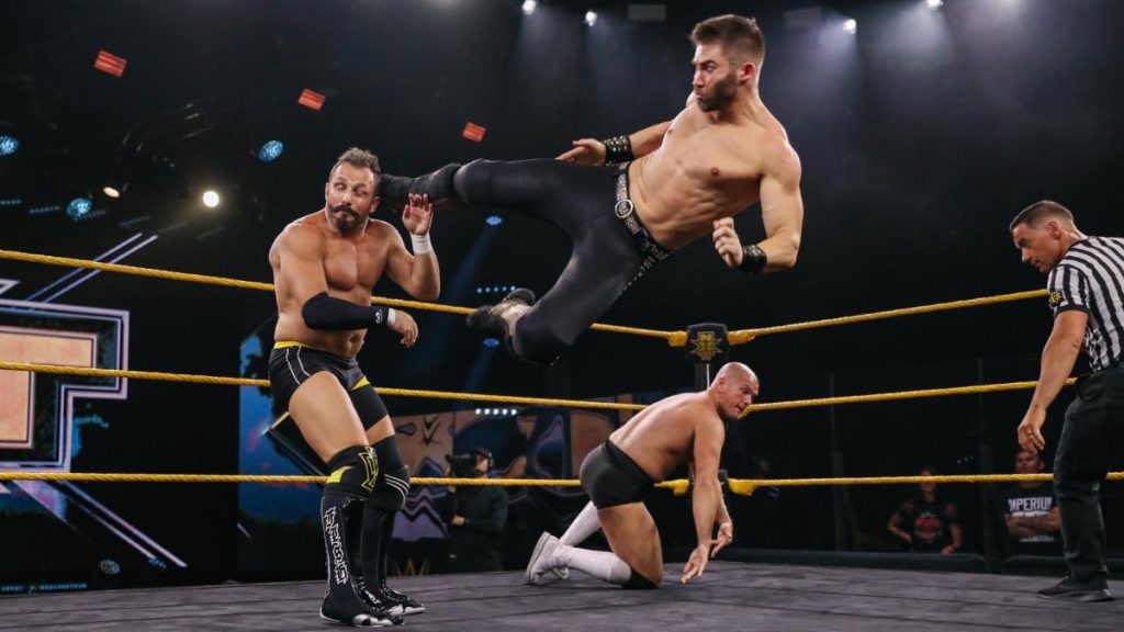 Tyler Breeze dropkicks Bobby Fish with Danny Burch in the background