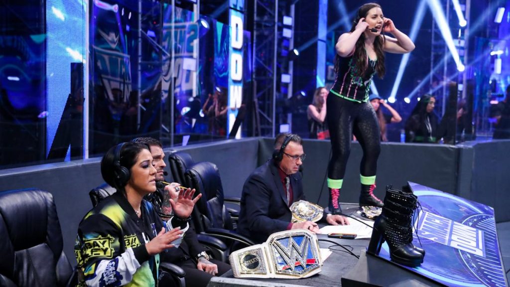 Nikki Cross and Bayley join commentary but Nikki chooses to stand on the desk.
