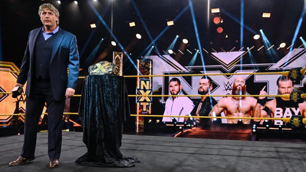 William Regal announces the NXT Championship Ironman match, with the belt beside him and the match graphic behind him