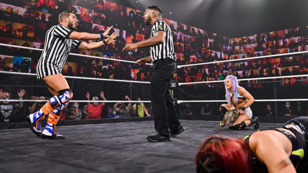 Johnny Gargano argues with the ref while Candice LeRae prepares to hit Io Shirai with the title belt