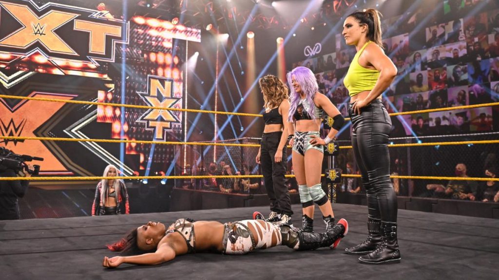 Candice LeRae Raquel Gonzalez, and Dakota Kai stand over Ember Moon in the ring, with Toni Storm looking on from ringside