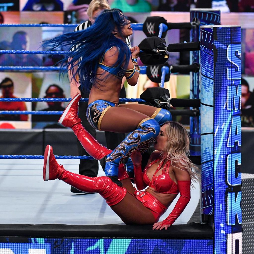 Sasha Banks delivers double knoees to Carmella against the ringpost.