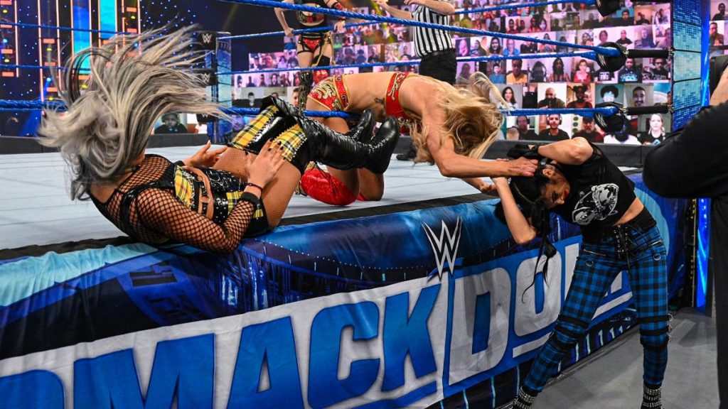 Liv Morgan dropkicks Charlotte Flair on the apron while Flair holds Billie Kay by the hair
