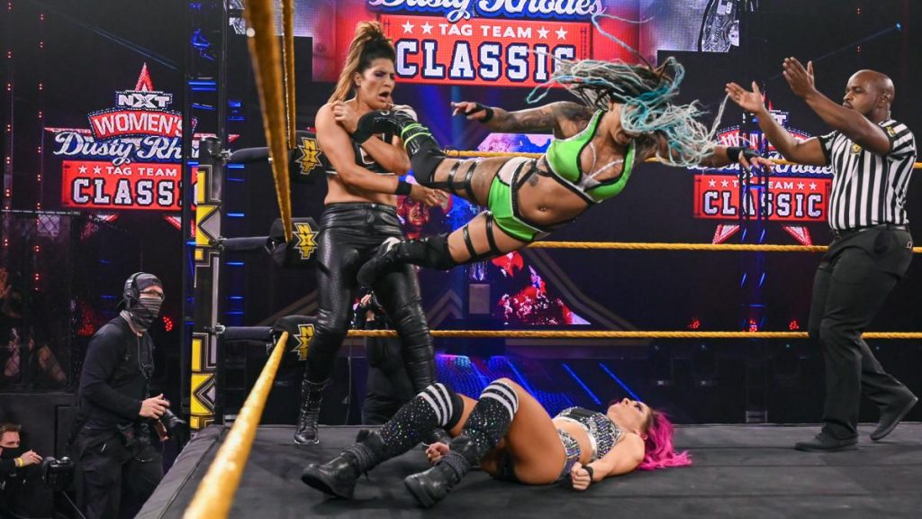 Dakota Kai lays on the mat as Kayden Carter dropkicks Raquel Gonzalez in the corner