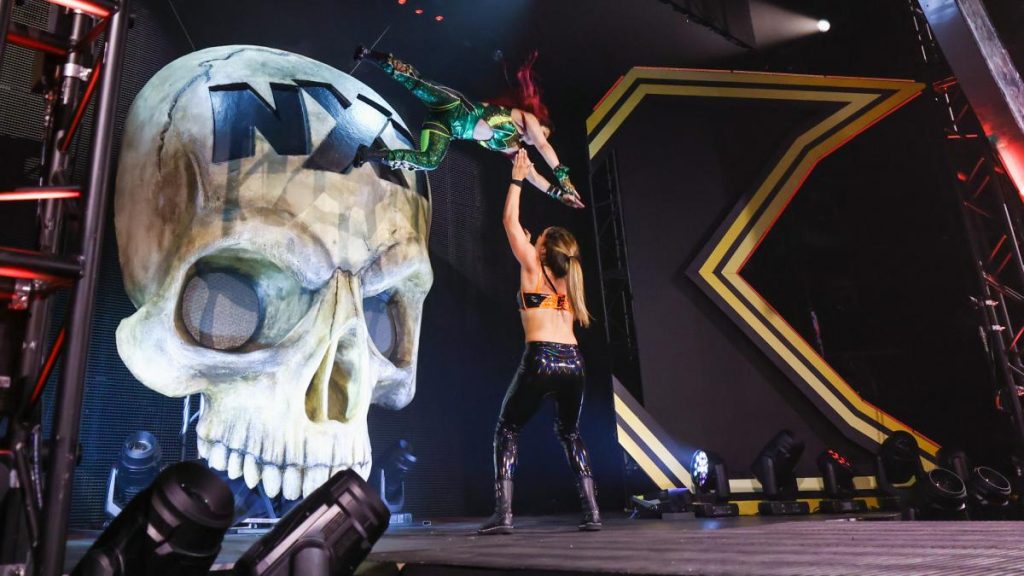 Io Shirai jumps off the big skull on the stage onto Raquel Gonzalez