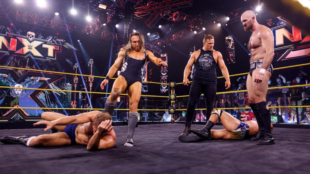 Pete Dunne, Ridge Holland, and Oney Lorcan stand over Timothy Thatcher and Tommaso Ciampa