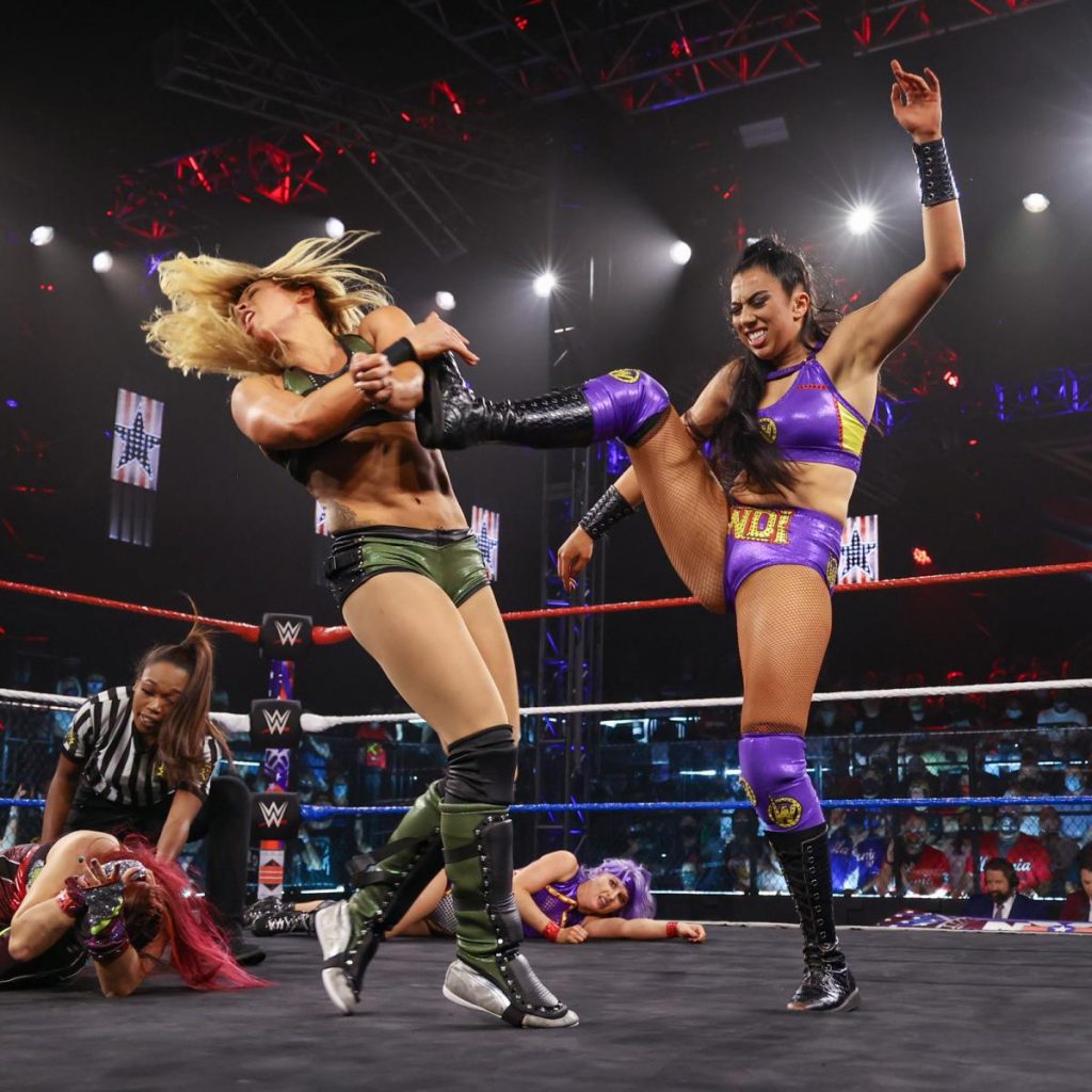 Indi Hartwell kicks Zoey Stark in the head, with Candice LeRae and Io Shirai laid out in the background