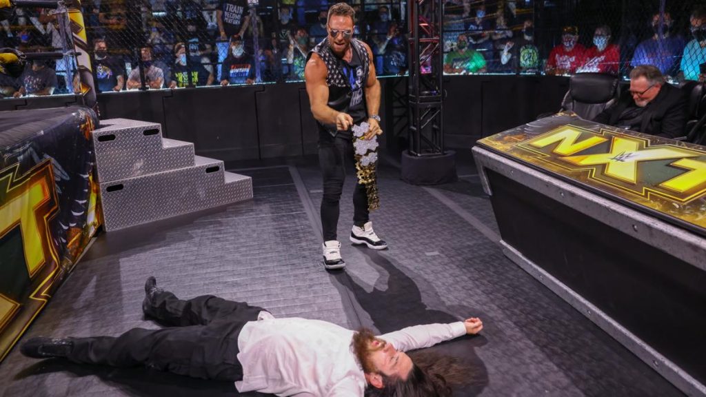 LA Knight stands over Cameron Grimes in front of the announce desk