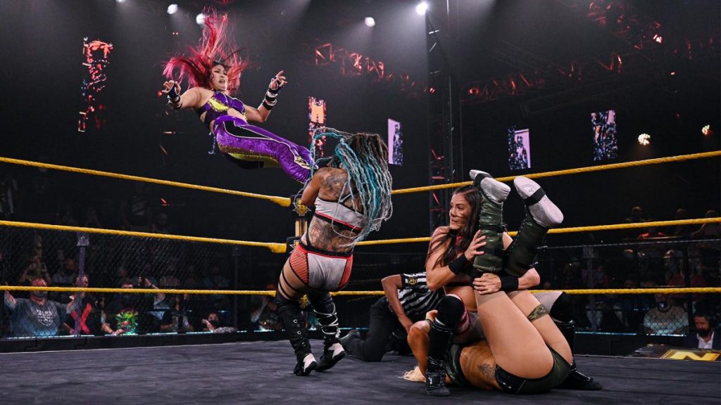 Io Shirai missile dropkicks Kayden Carter onto Kacy Catanzaro to stop her pinning Zoey Stark