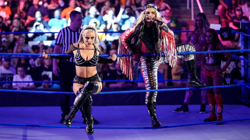 Liv Morgan and Toni Storm pose on the ropes with Zelina Vega and Carmella in the background.