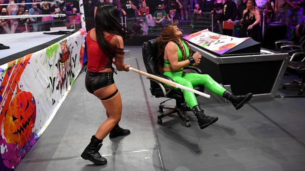 Raquel Gonzalez, sat in an announce chair being hit with a kendo stick by Mandy Rose