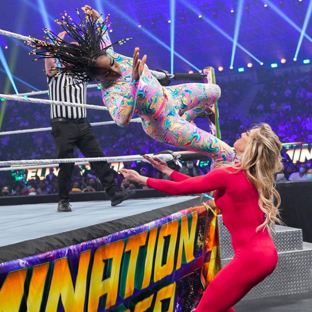 Naomi barrels over the top rope onto Charlotte Flair