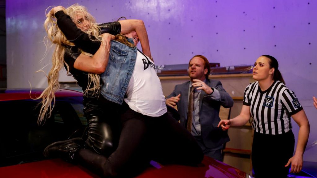 Charlotte Flair with Ronda Rousey in hold on a car bonnet